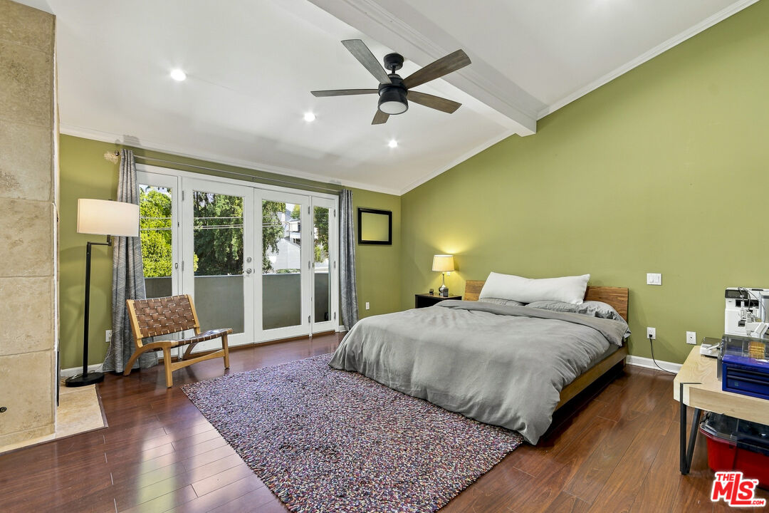 Bedroom with a large bed, green walls, hardwood floors, and white French doors opening to a balcony.
