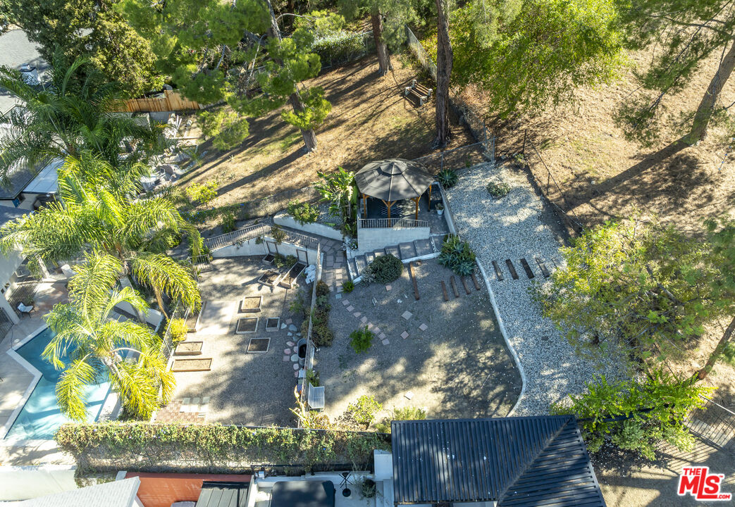 Aerial backyard with a swimming pool, patio seating, gazebo, and wooded hillside.