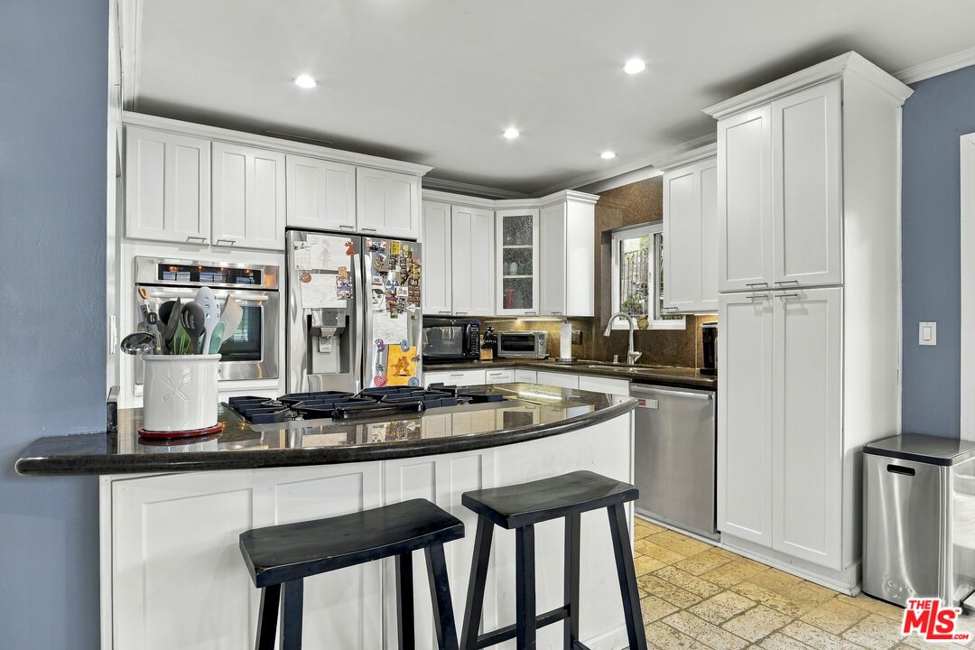 Kitchen with white cabinetry, dark granite peninsula, built-in cooktop, and stainless steel appliances.