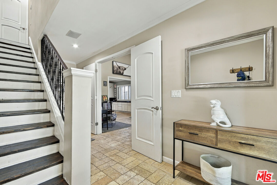 Entry hall with a dark-trimmed staircase, tiled floor, and console table beneath a large mirror.