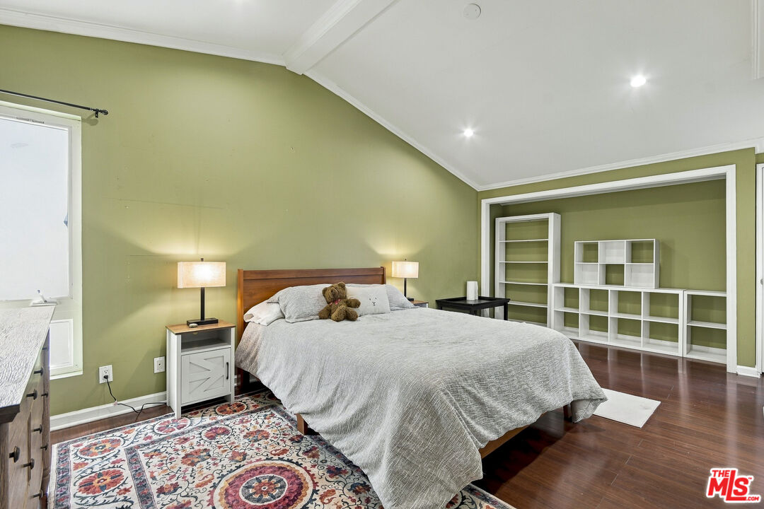 Bedroom with a large bed, olive-green walls, high angled ceiling, and white built-in shelving.
