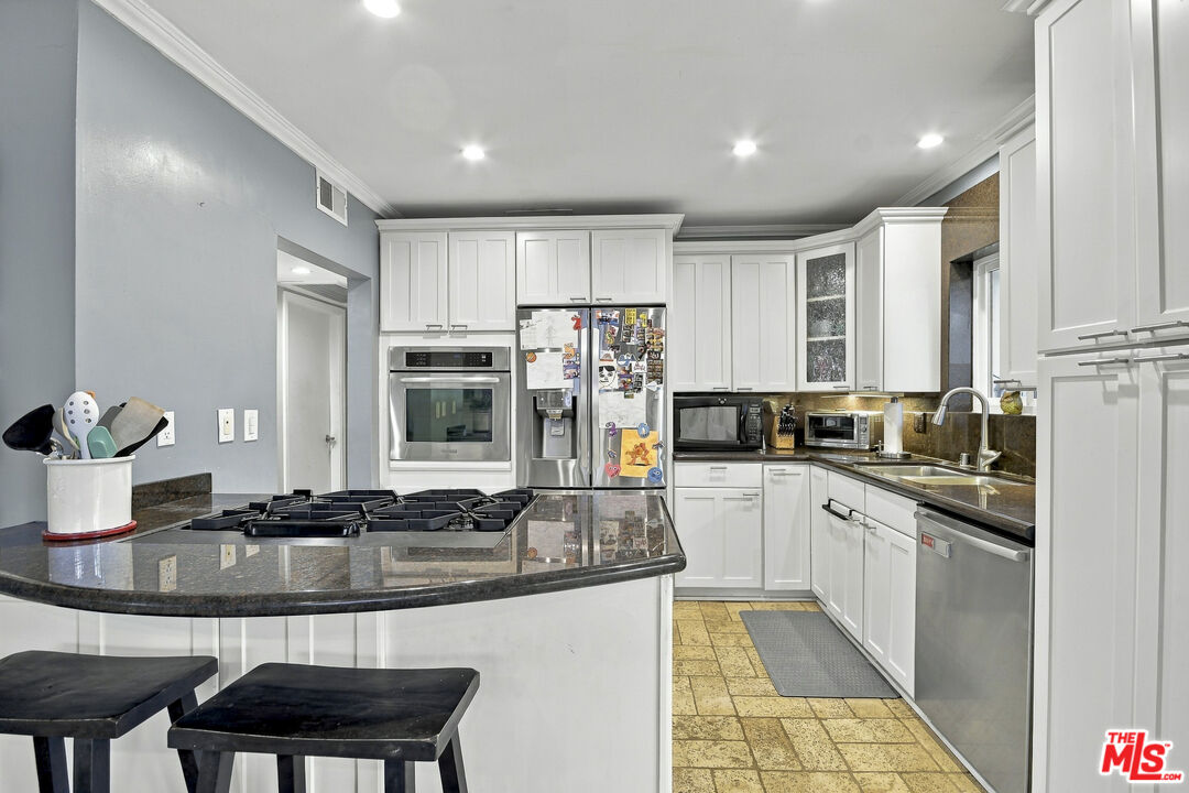 Kitchen with white cabinets, granite island and gas cooktop, stainless steel appliances, and tan tile flooring.