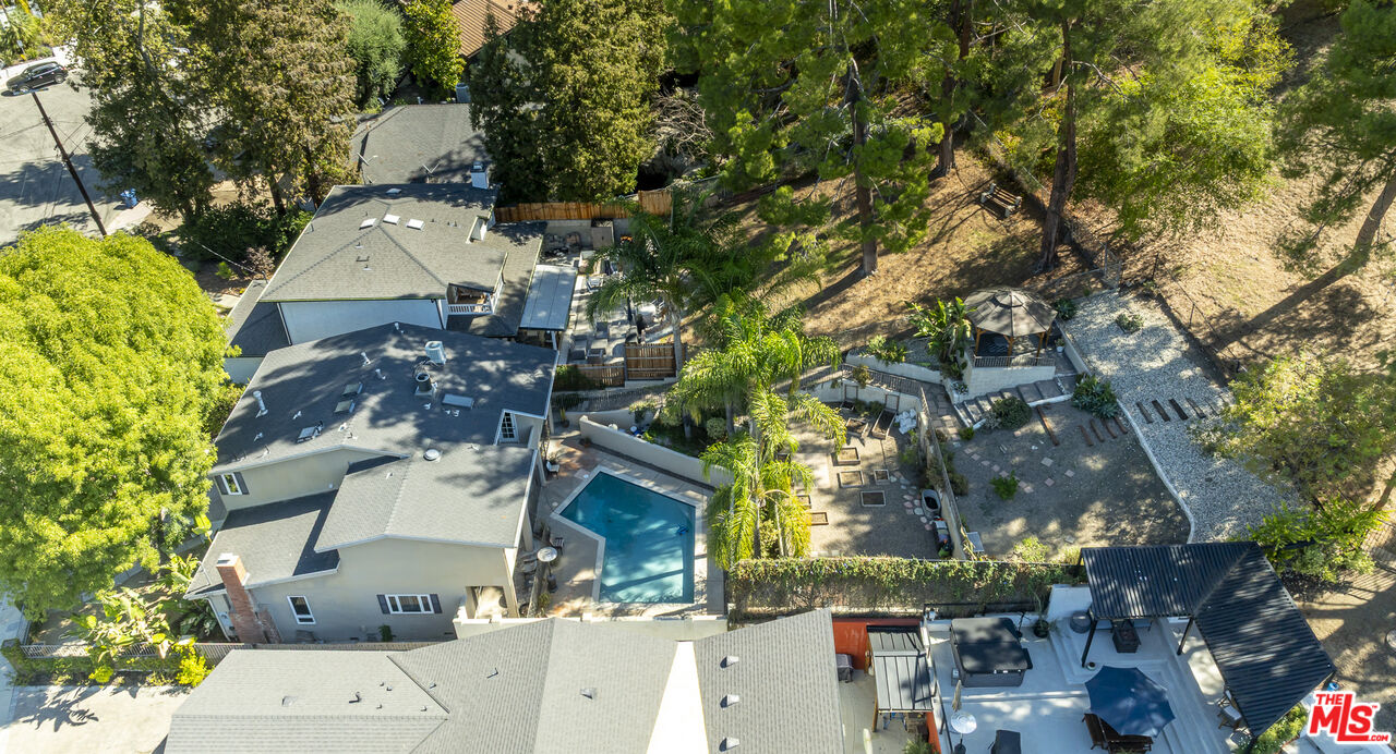 Aerial view of a house with a swimming pool, landscaped yard, and wooded hillside.