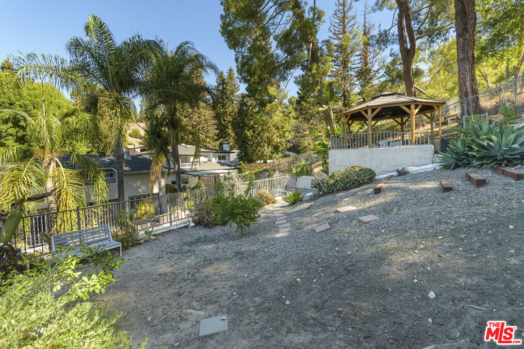 Sloped backyard with a raised gazebo, gravel yard, stepping stones, and mature trees.