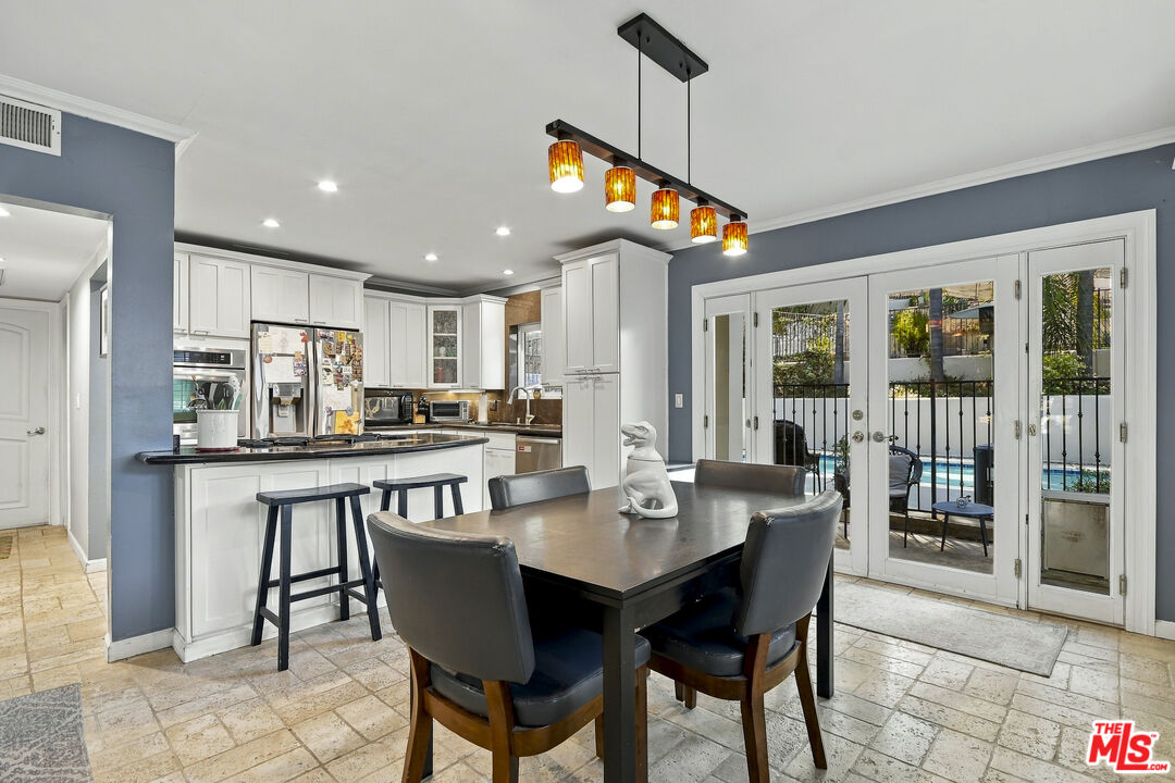 Kitchen and dining area with white cabinets, a dark dining table, and glass doors overlooking a pool.