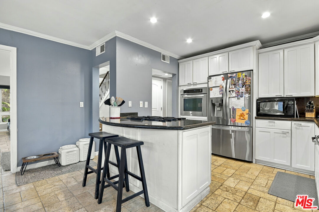 Kitchen with a central island, white cabinetry, stainless steel appliances, and tan tile flooring.
