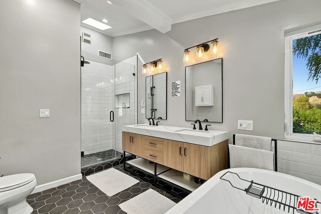 Remodeled bathroom with a double wood vanity, glass shower, and soaking tub beside a window.
