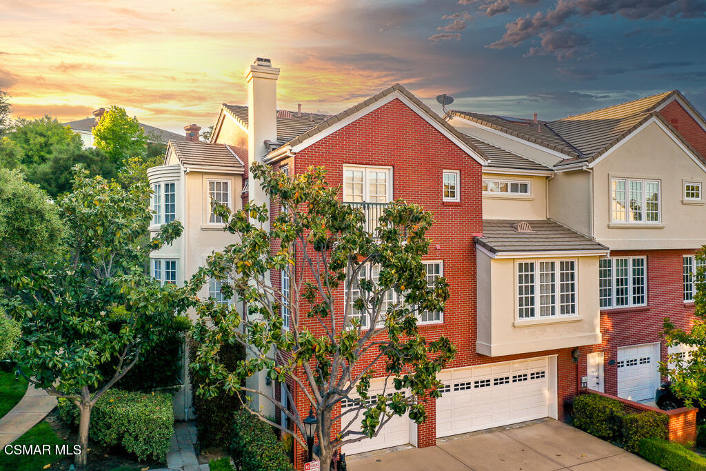 Red-brick and cream stucco residence with tiled roofs and mature trees at sunset.