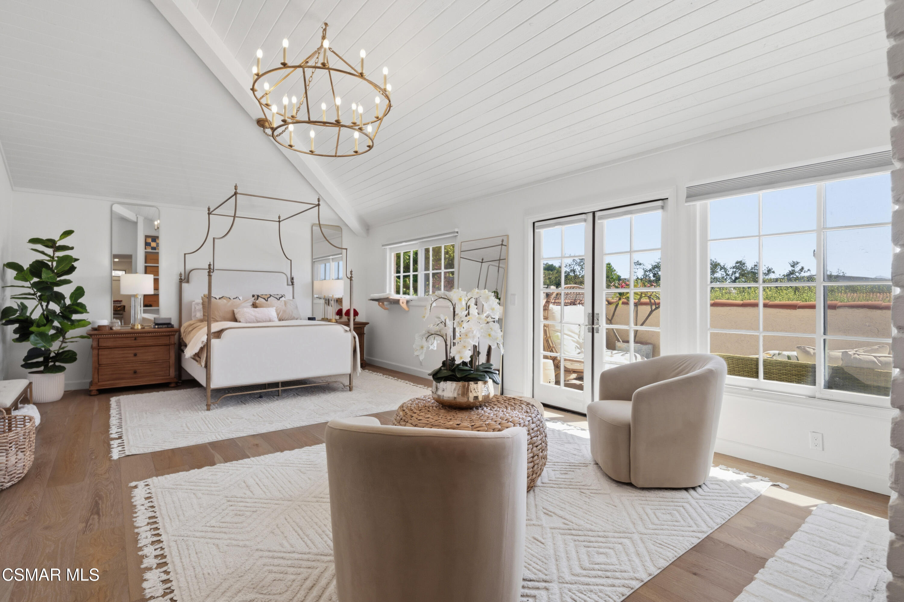 Bright bedroom with a canopy bed, vaulted ceiling, and large windows opening onto a patio.