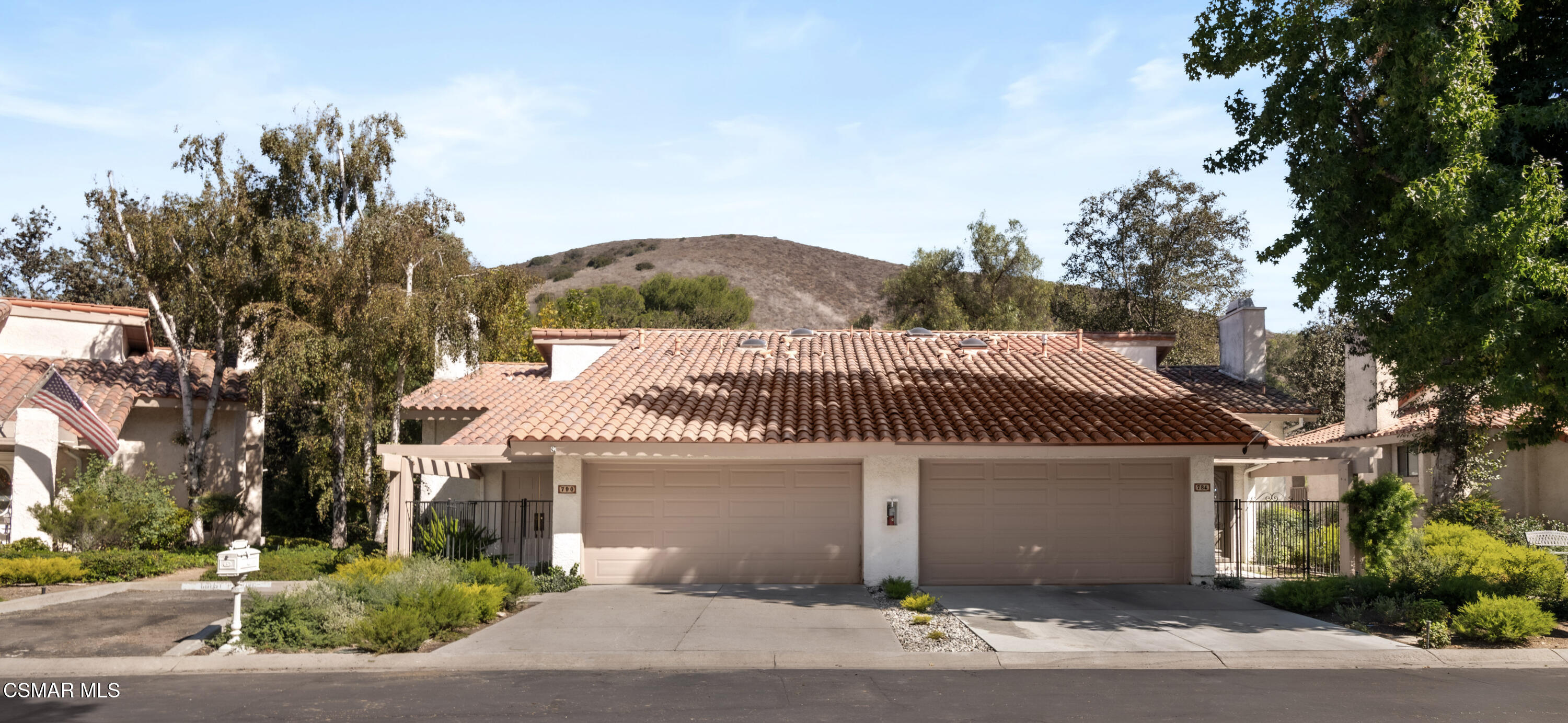 Tan stucco home with a terracotta tile roof, two garage doors, gated entry, and landscaped frontage.