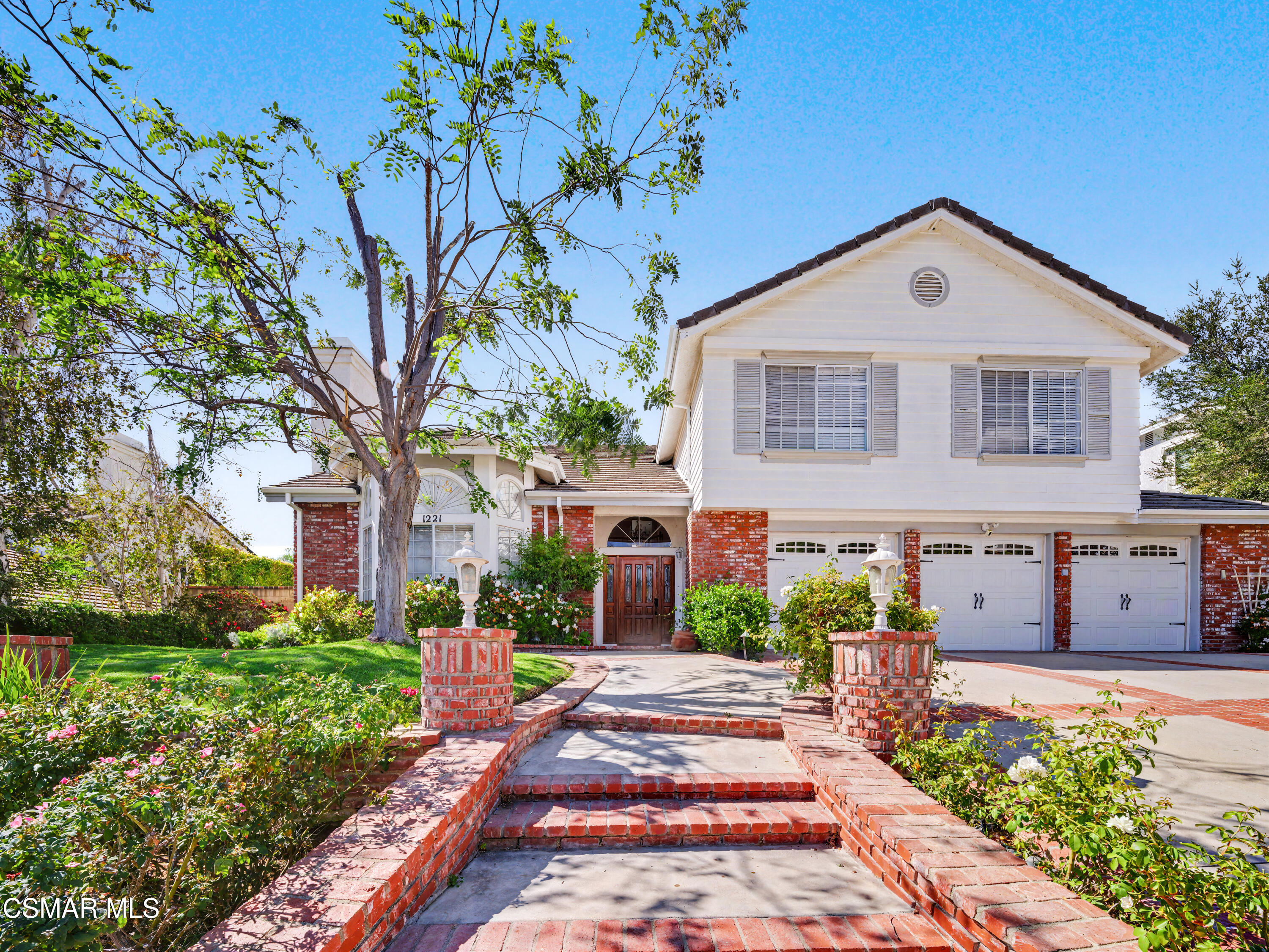 Two-story white and red-brick home with a three-car garage and landscaped brick entry.