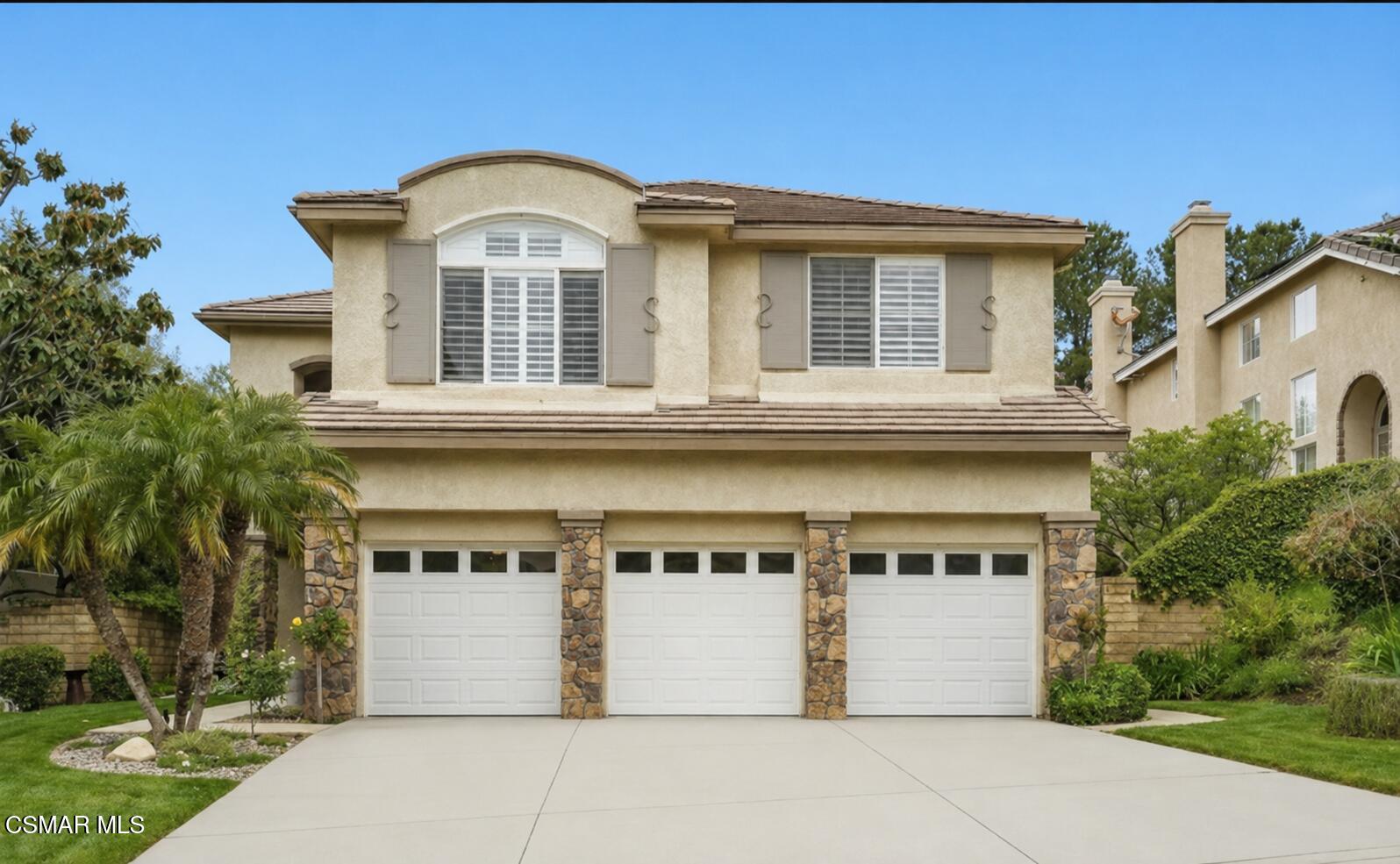 Two-story stucco house with three garage doors, stone accents, and landscaped front yard.