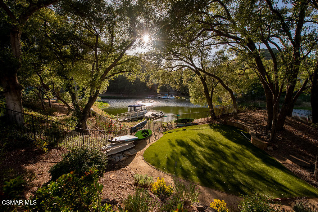 Lakeside backyard with a curved turf lawn, mature trees, kayaks, and a small dock.