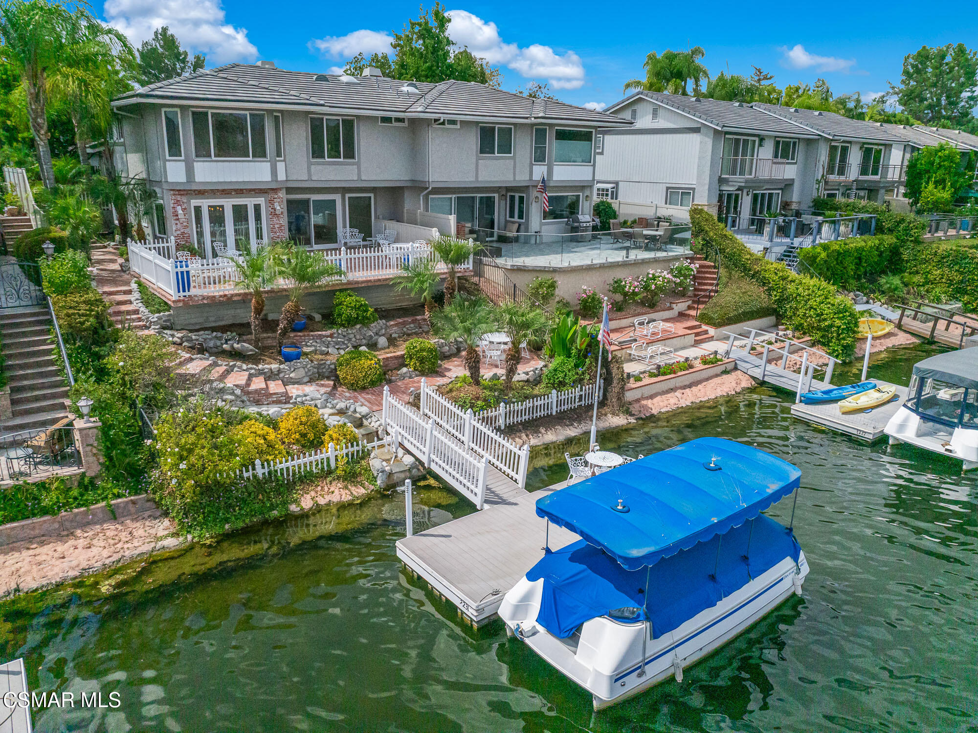 Waterfront homes line a canal, with landscaped yards, private docks, and a covered pontoon boat.
