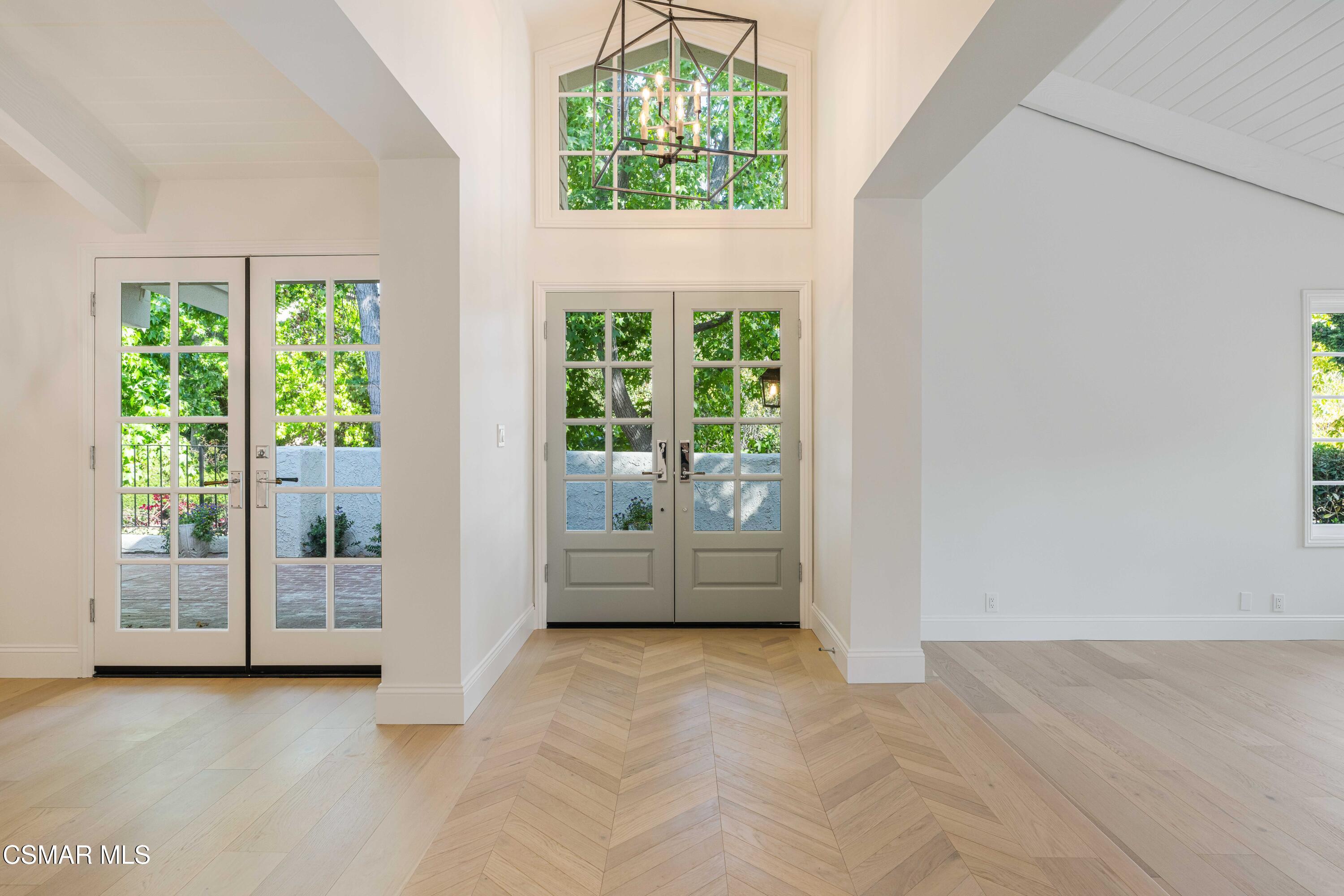 Vacant entryway with glass-paneled double doors, herringbone flooring, and a geometric chandelier.