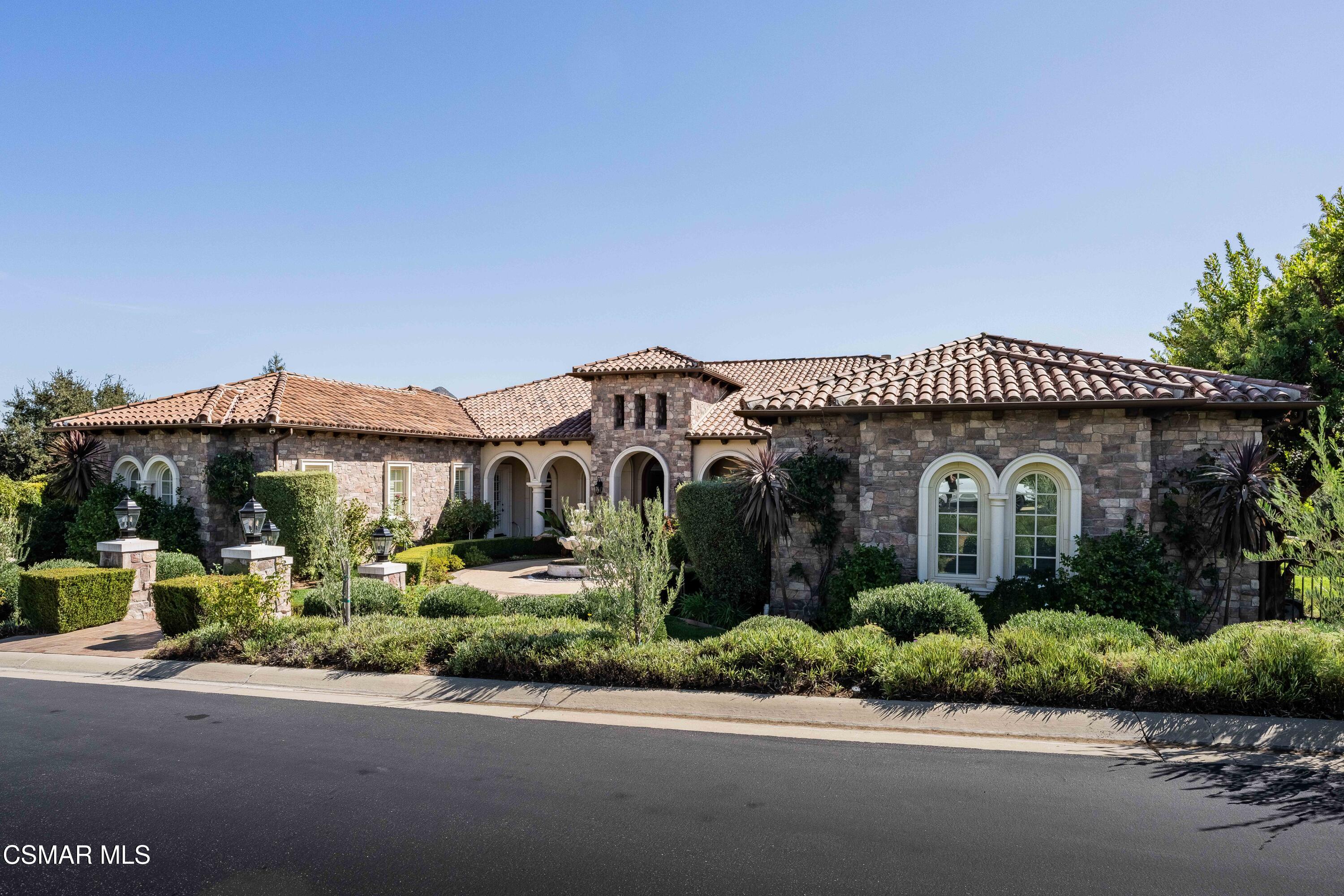 Stone residence with a terracotta tile roof, arched entryways, and manicured landscaping.