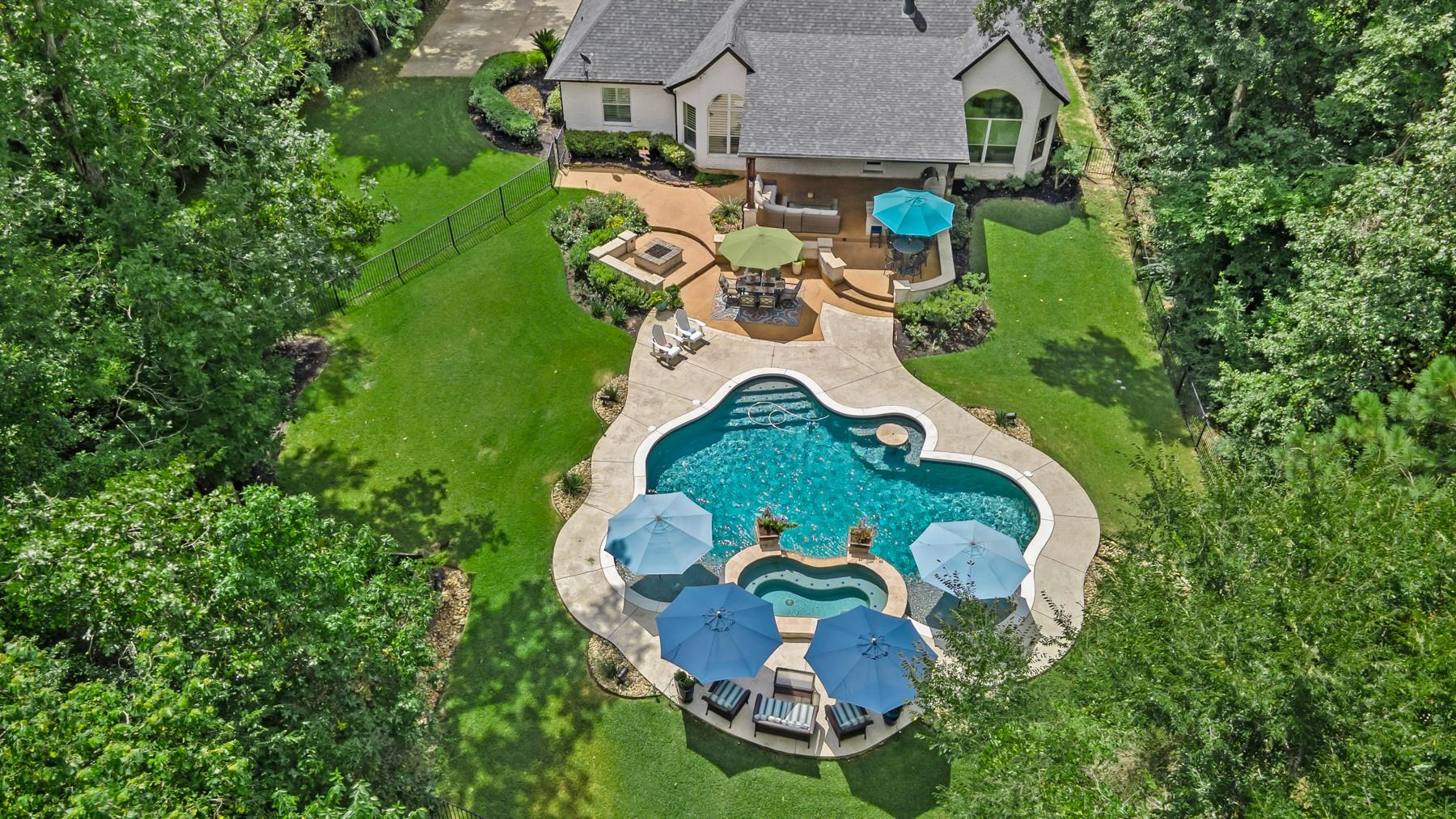 Aerial view of a landscaped backyard with a freeform pool, patio seating, and mature trees.