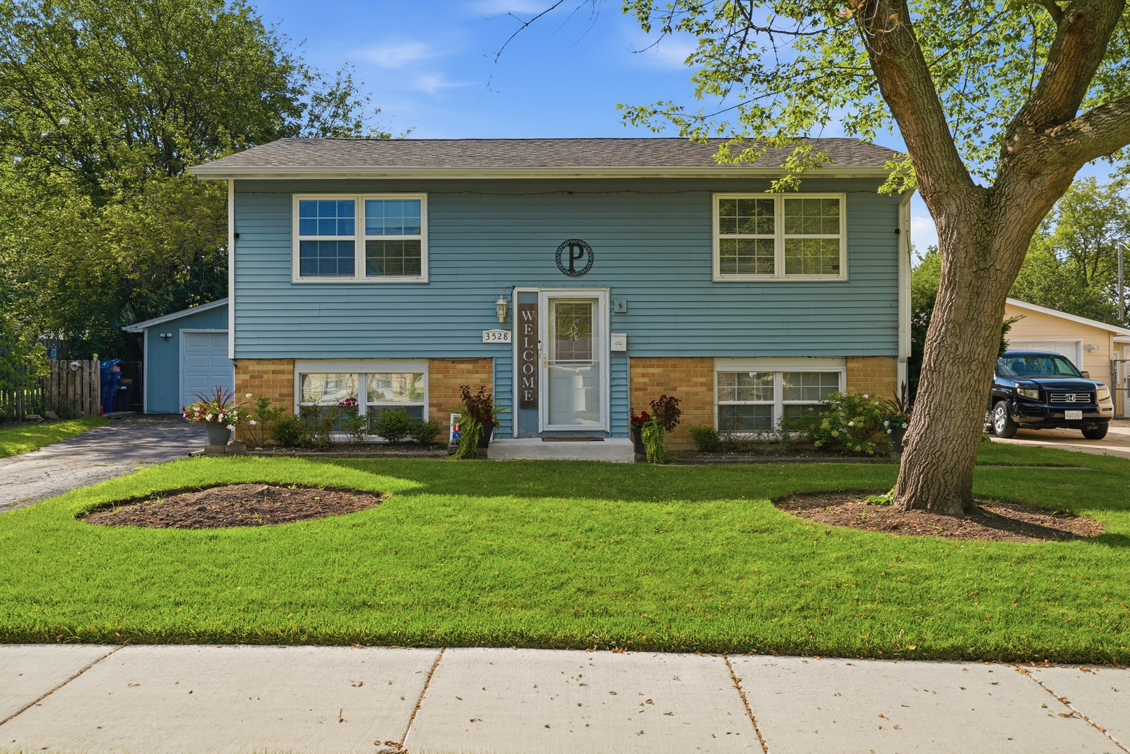 Blue split-level house with brick lower walls, white-trimmed windows, and a large tree in the front yard.