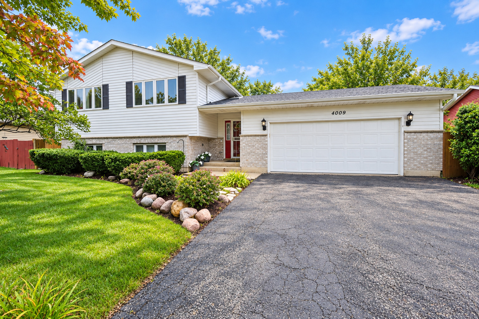 White split-level home with a brick facade, red front door, attached garage, and landscaped front yard.