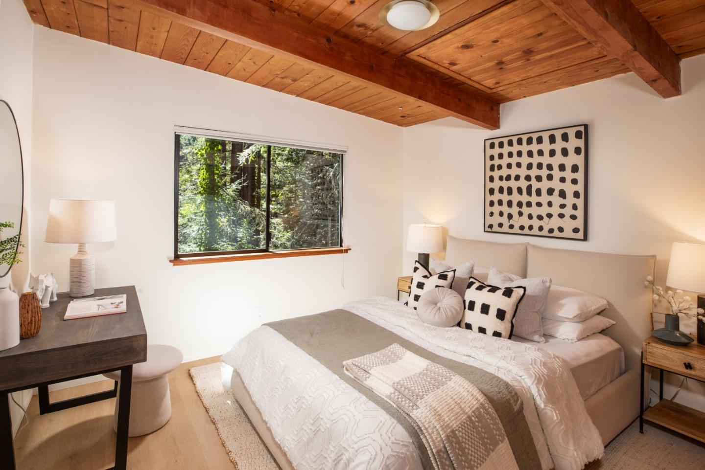 Bedroom with a large neutral bed beneath a wood-plank ceiling, overlooking leafy trees.