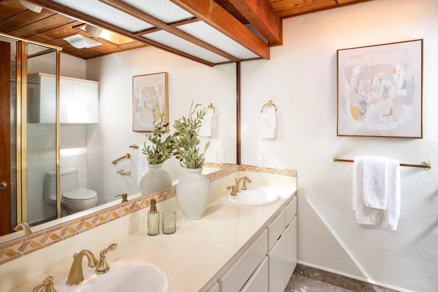 Bathroom with a double-sink vanity, brass fixtures, and exposed wooden ceiling beams.
