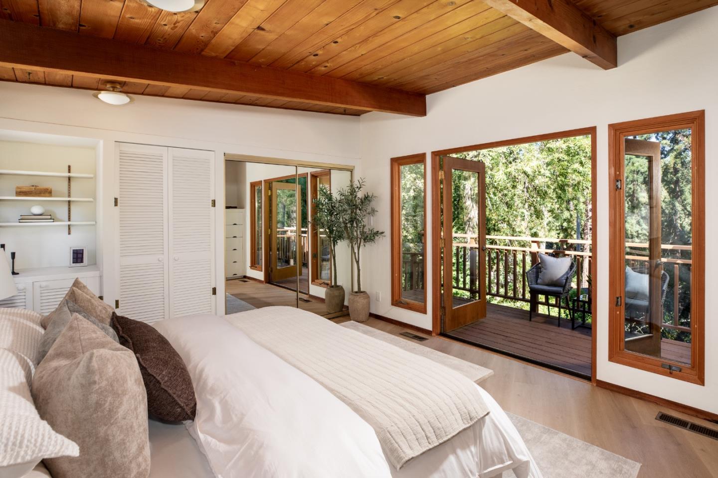 Bedroom with a wood plank ceiling and glass doors opening to a tree-surrounded deck.