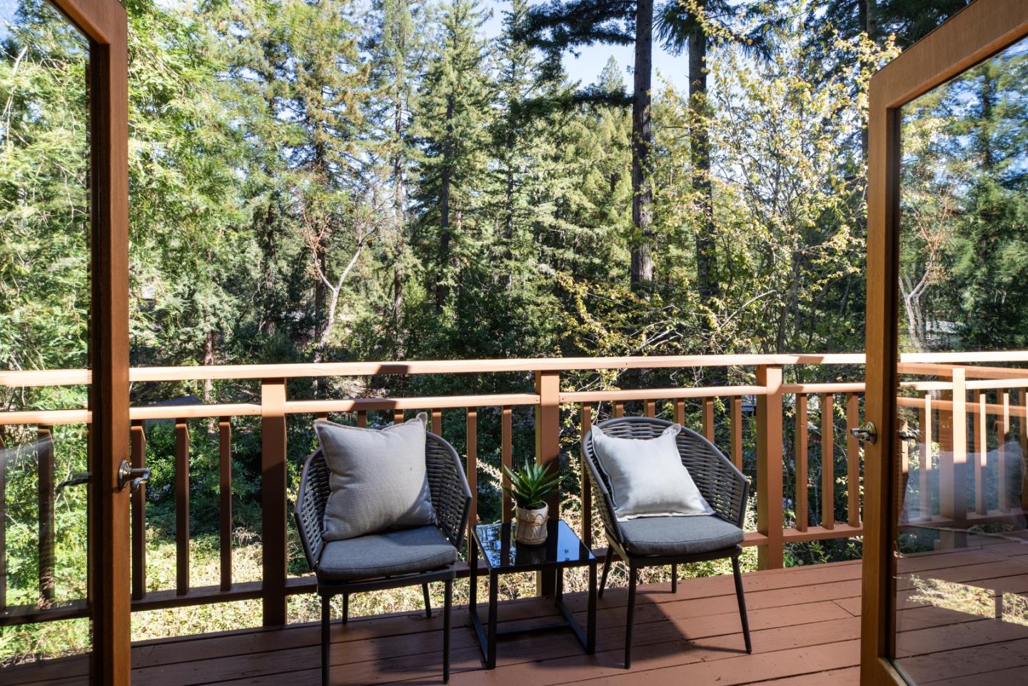 Wooden deck with cushioned chairs and a small table overlooking dense woodland.