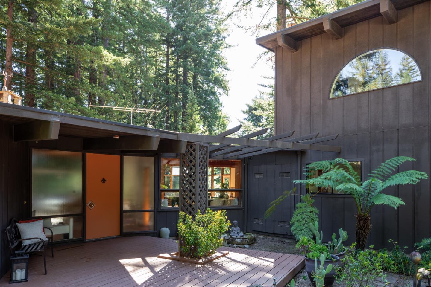 Wooded home courtyard with a redwood deck, pergola, and arched window.