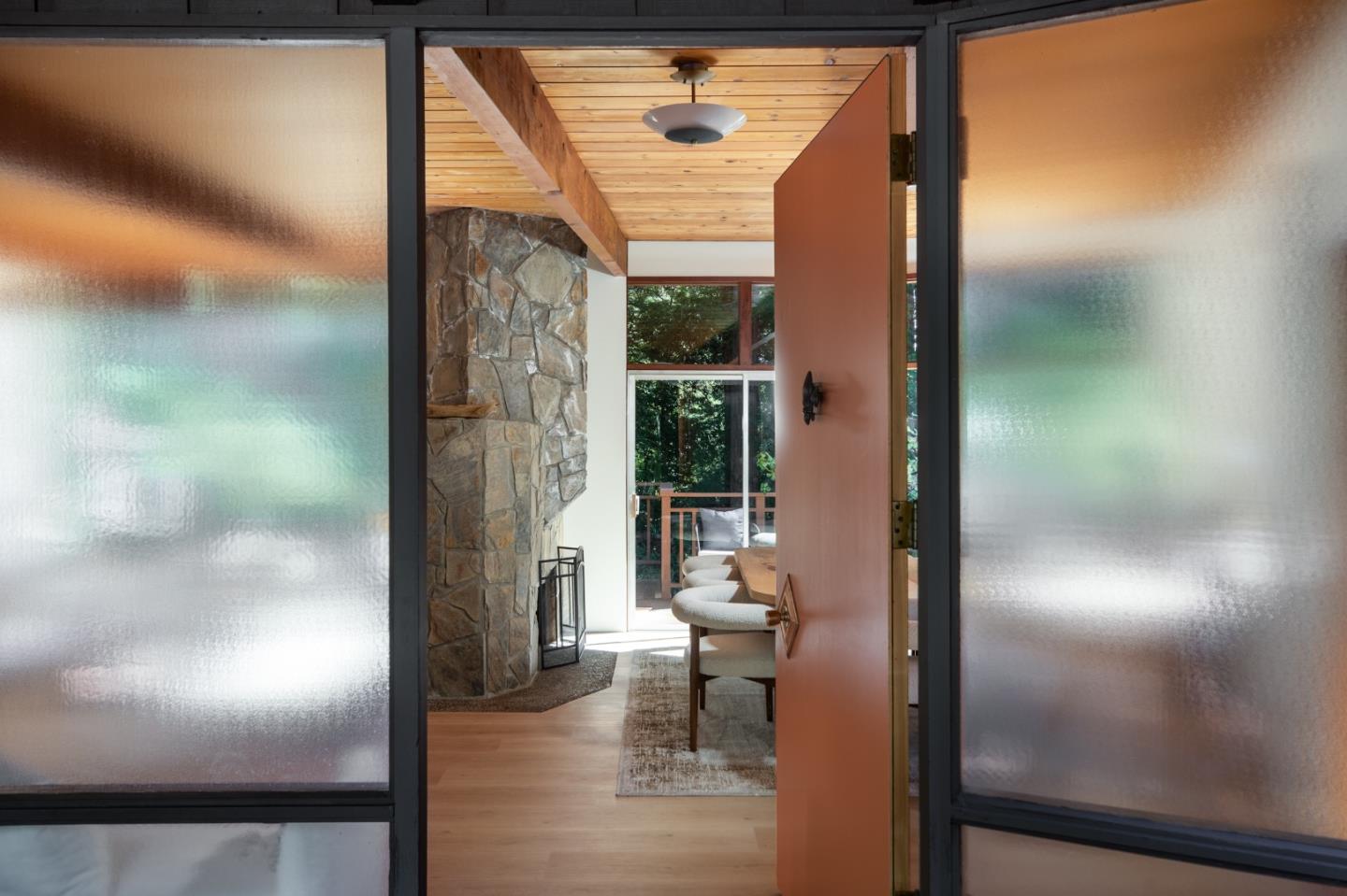 Home entry with a stone fireplace, exposed wood ceiling beam, and open front door.