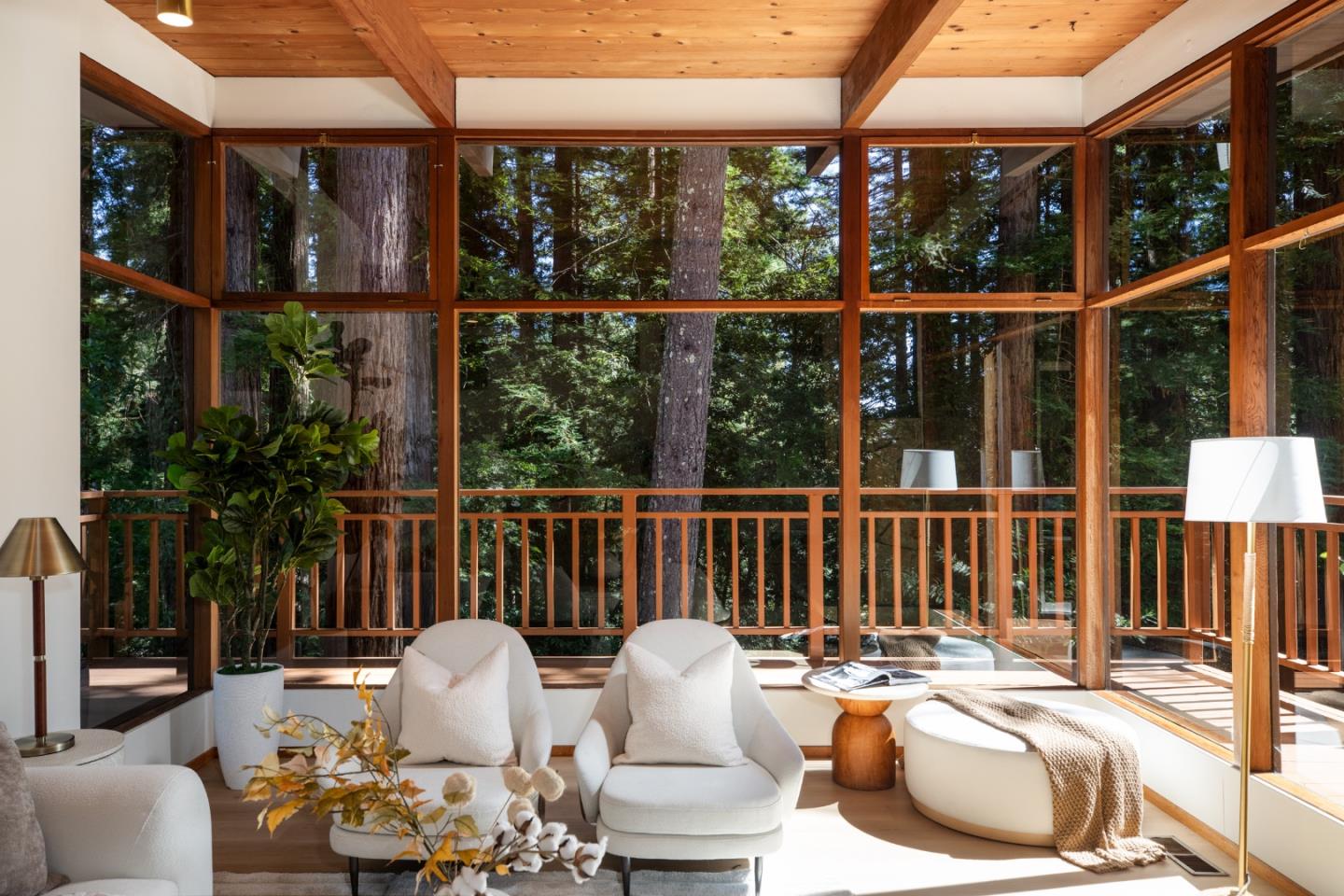 Living room with floor-to-ceiling windows overlooking trees and a warm wood-beamed ceiling.