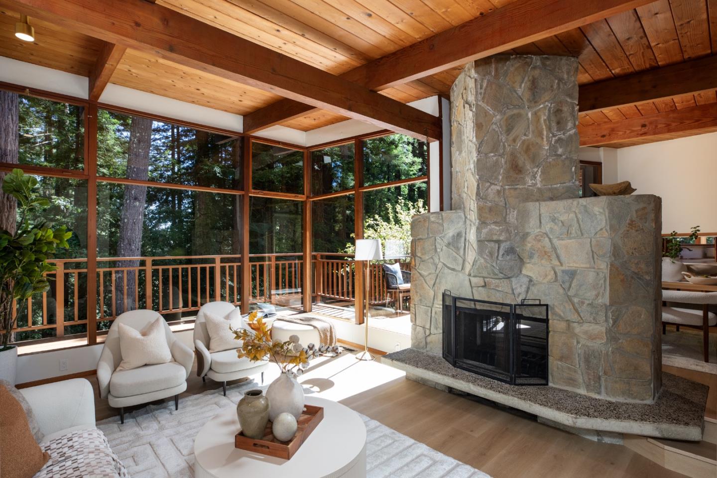 Living room with a vaulted wood ceiling, massive stone fireplace, and windows overlooking the woods.