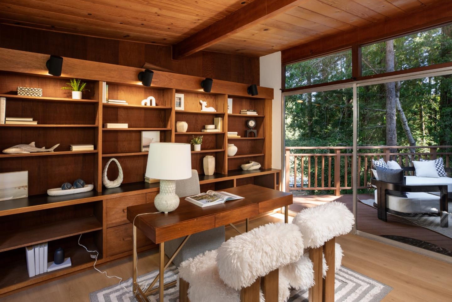 Wood-paneled study with built-in bookshelves, a desk, and windows overlooking a tree-lined deck.