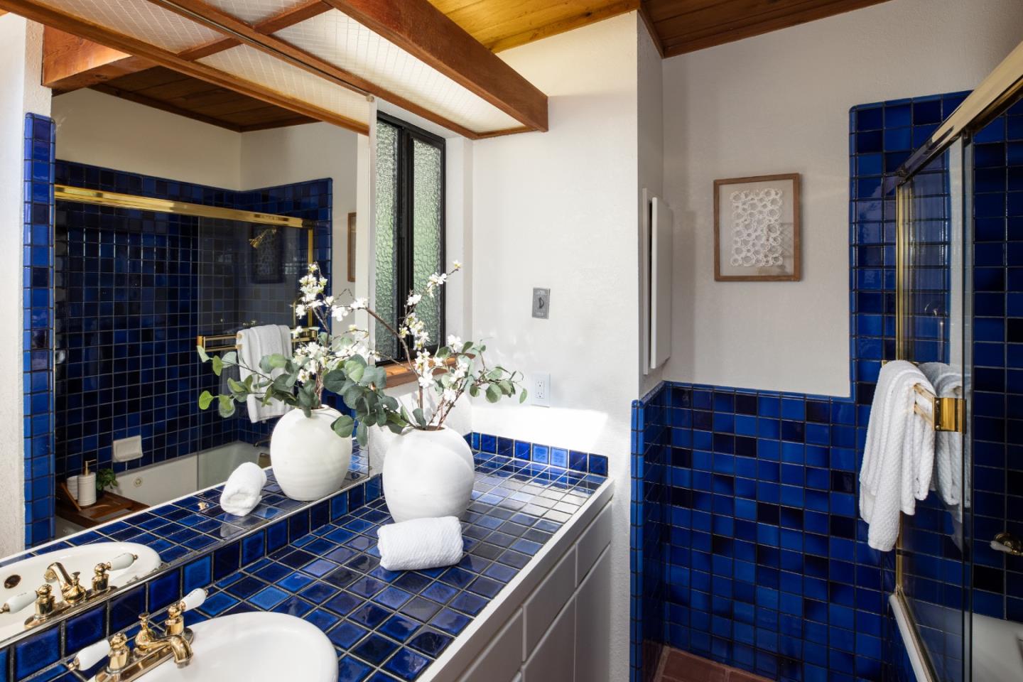 Bathroom with deep blue tile, two white vessel sinks, and exposed wood ceiling beams.