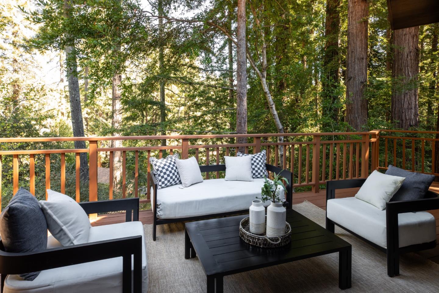 Furnished deck overlooking a redwood forest, with black-and-white seating and a dark coffee table.