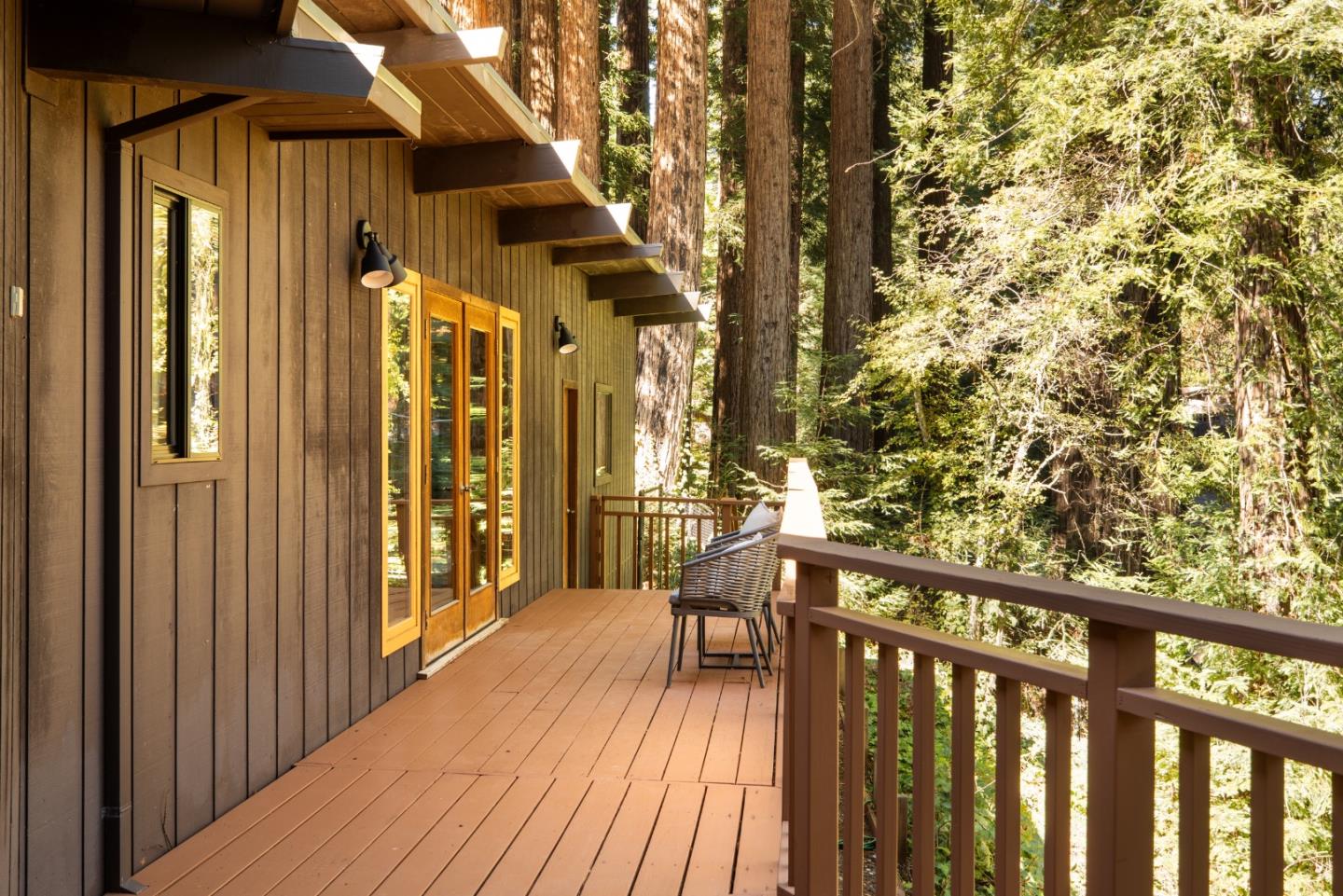 Wooden deck beside a wood-sided home, overlooking a sunlit forest.