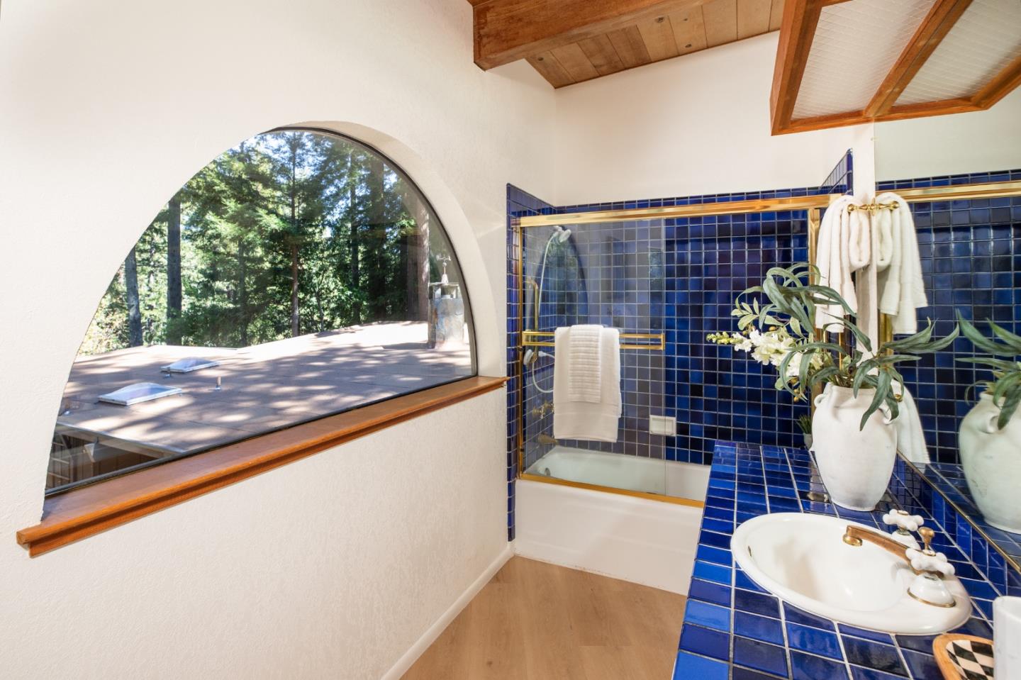 Bathroom with blue tile, a white sink, and an arched window overlooking trees.