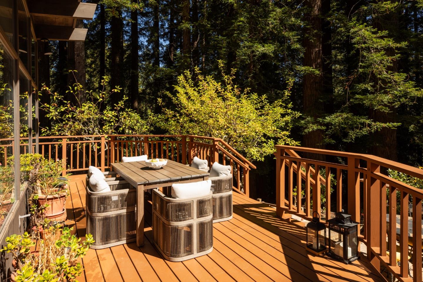 Furnished wood deck with dining table and chairs surrounded by forest trees.