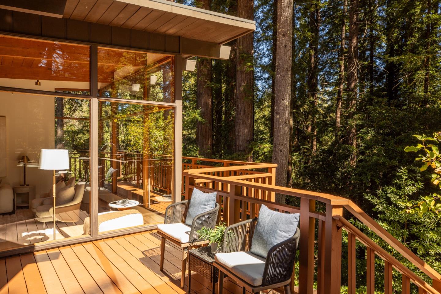 Furnished wooden deck beside floor-to-ceiling glass doors, surrounded by tall redwood trees.