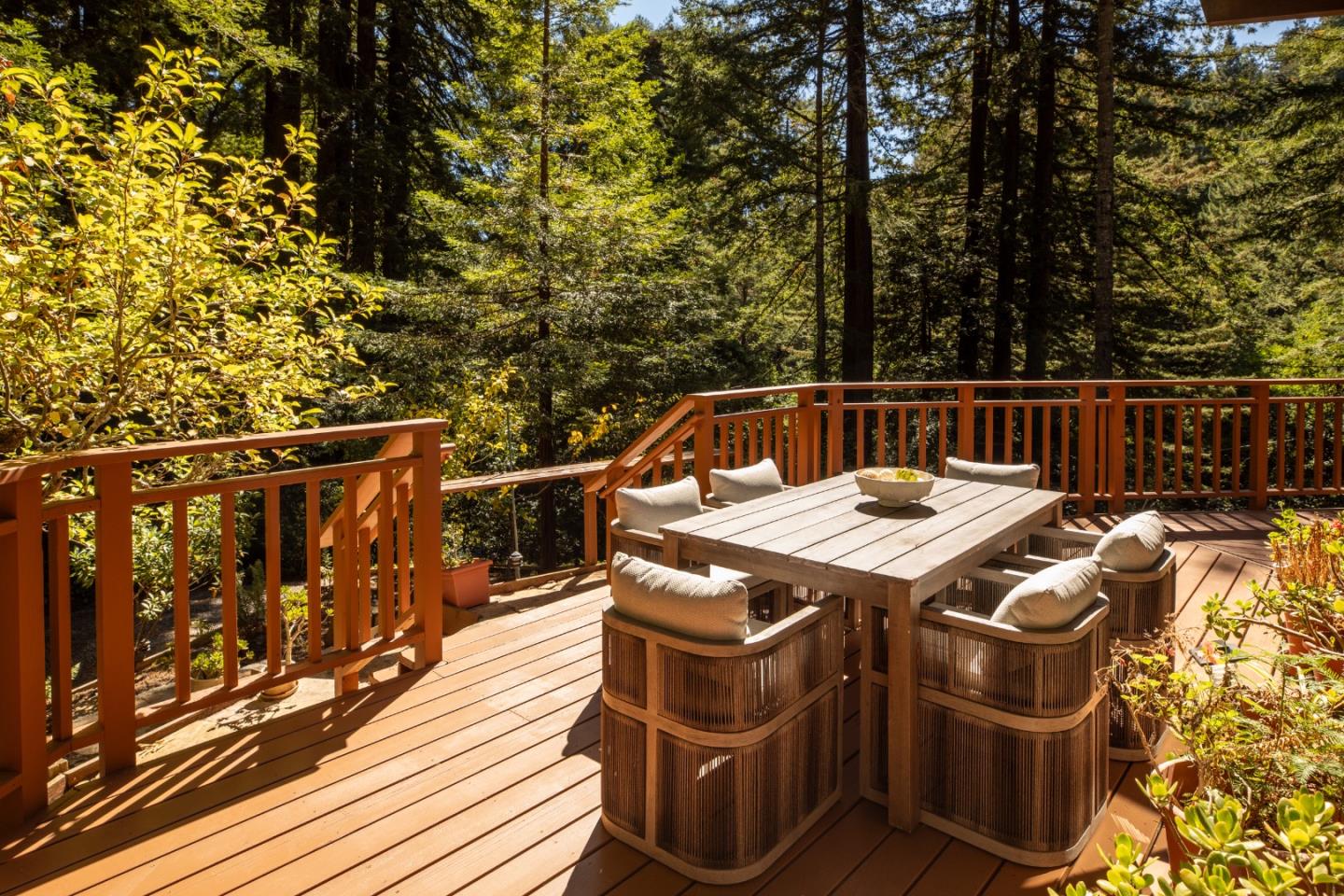 Woodland deck with a wooden dining table, cushioned chairs, and stairs.