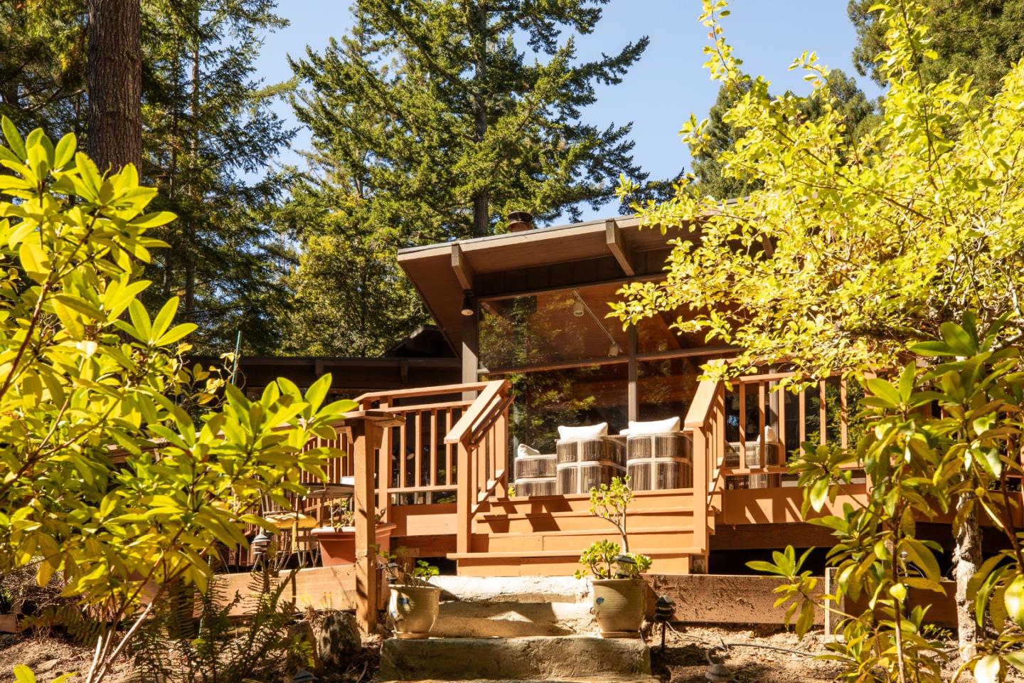 Woodland home with a raised timber deck, broad windows, and stone steps through the garden
