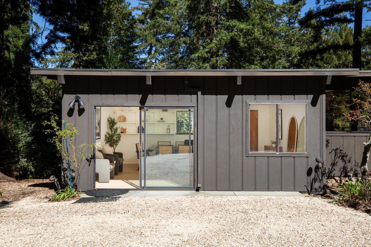 Modern gray wood-sided home with a broad roofline, sliding glass doors, and wooded surroundings.