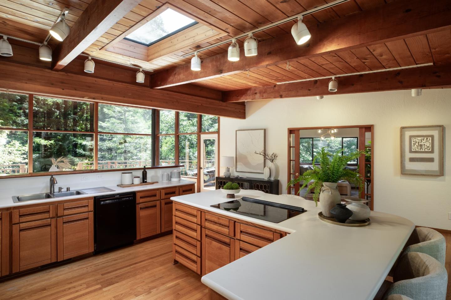 Kitchen with a large white cooktop island, wood-plank ceiling, skylight, and windows overlooking trees.