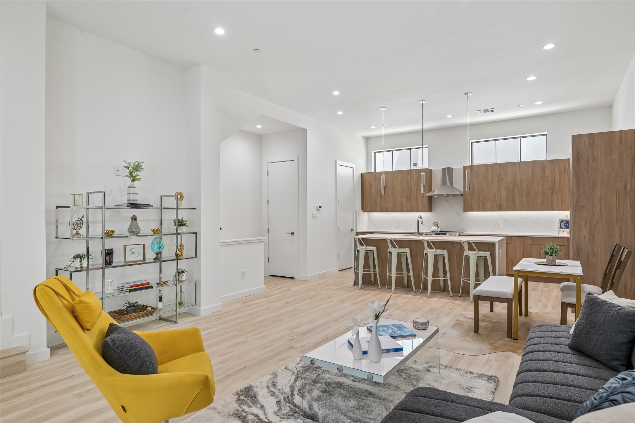 Open-plan living room and kitchen with wood cabinetry, a gray sofa, and a mustard-yellow armchair.