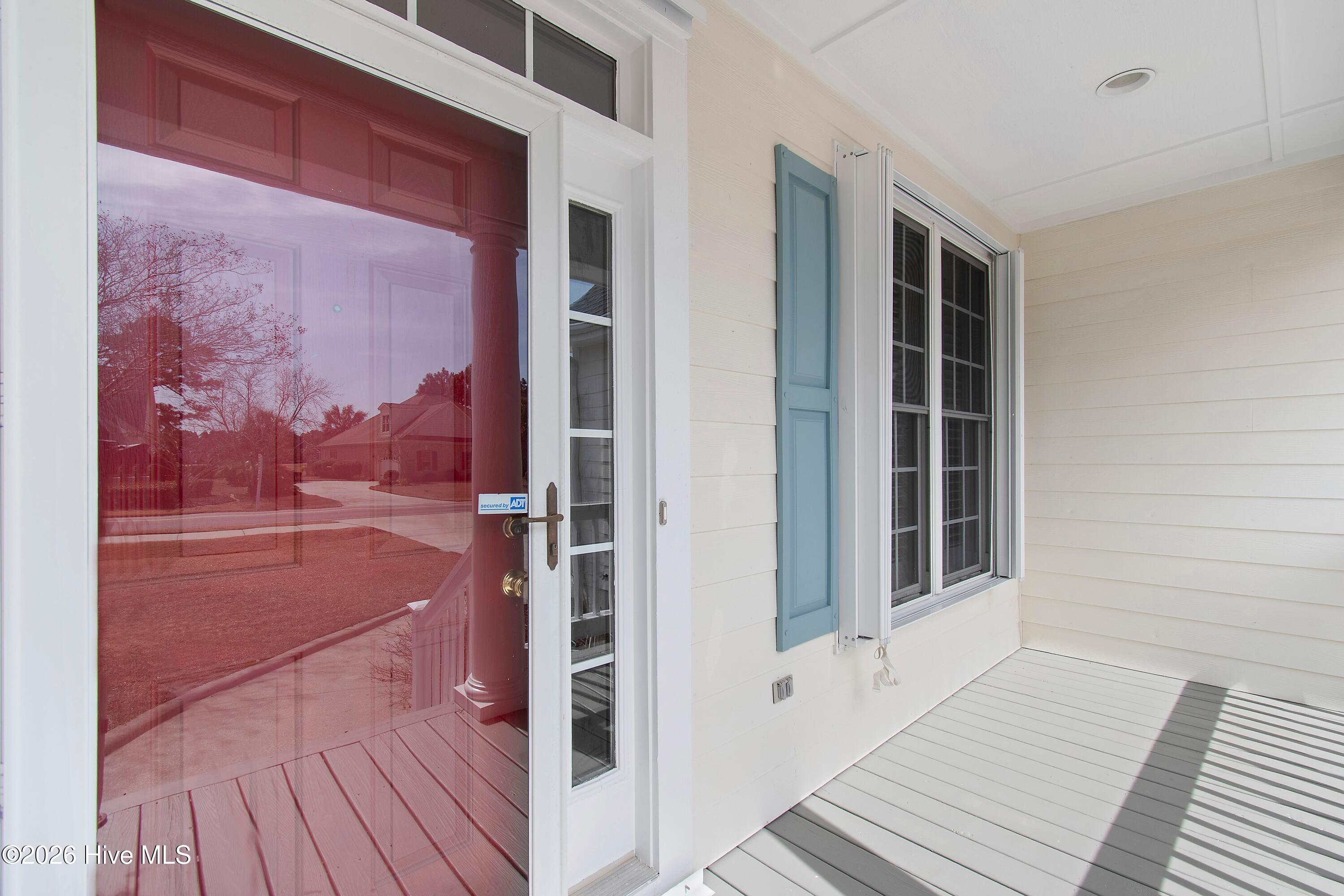 Covered porch with gray decking, white siding, blue shutter, and reflective glass storm door.