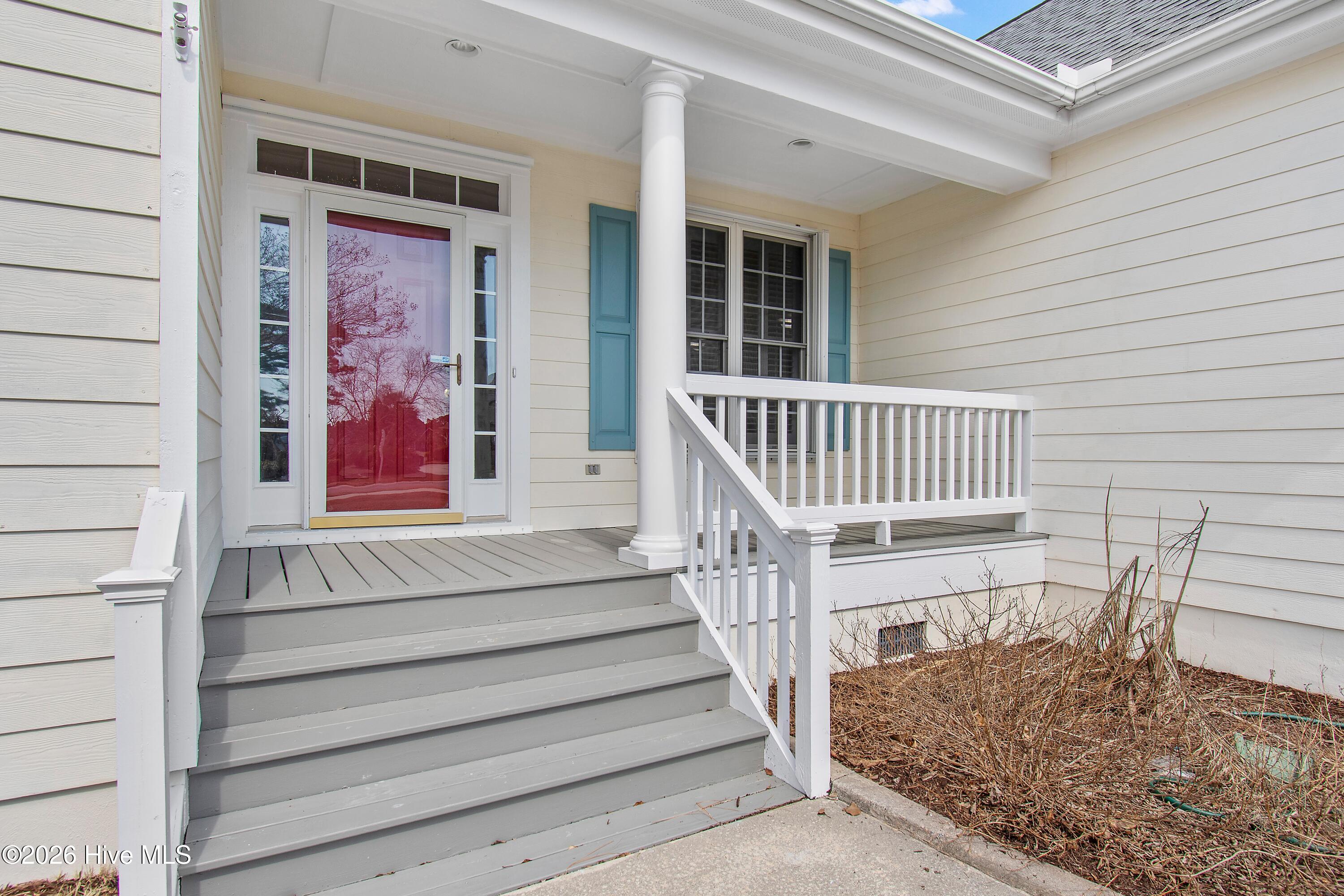 Covered front porch with gray steps, white railings, glass door, and teal shutters.