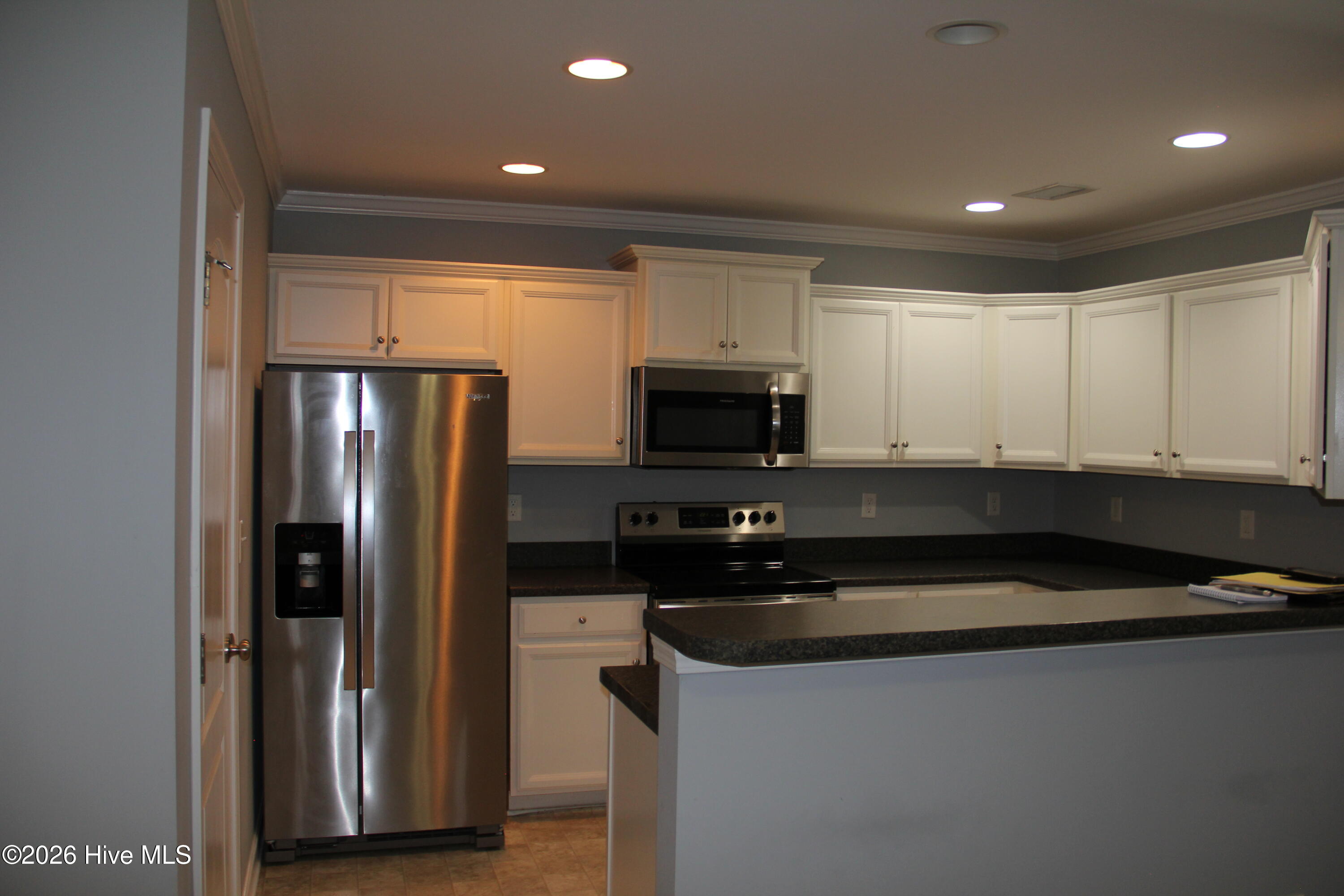 Kitchen with white cabinets, stainless-steel appliances, and a dark countertop peninsula.