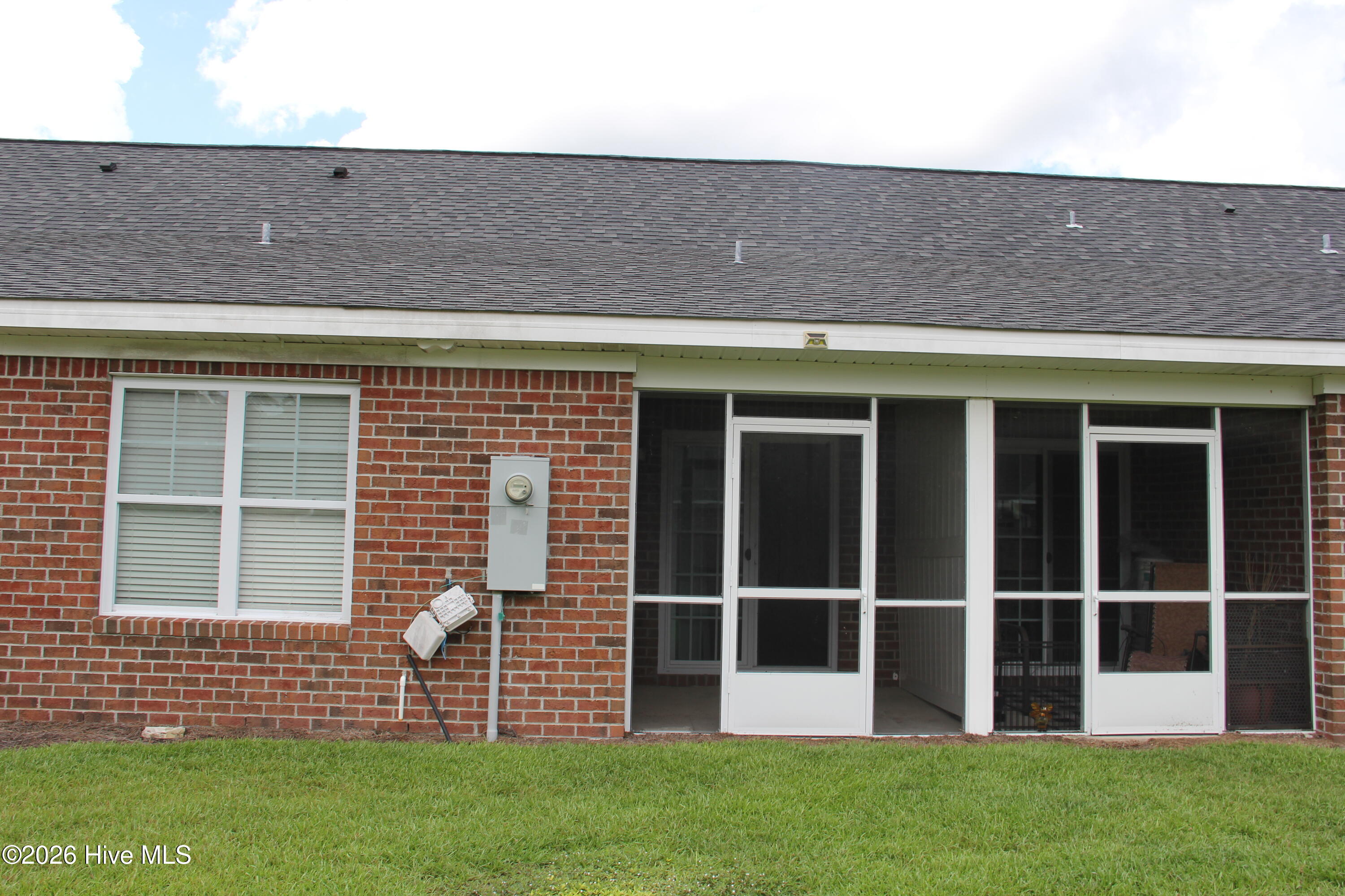 Brick home’s rear exterior with a white-framed screened porch and green lawn.