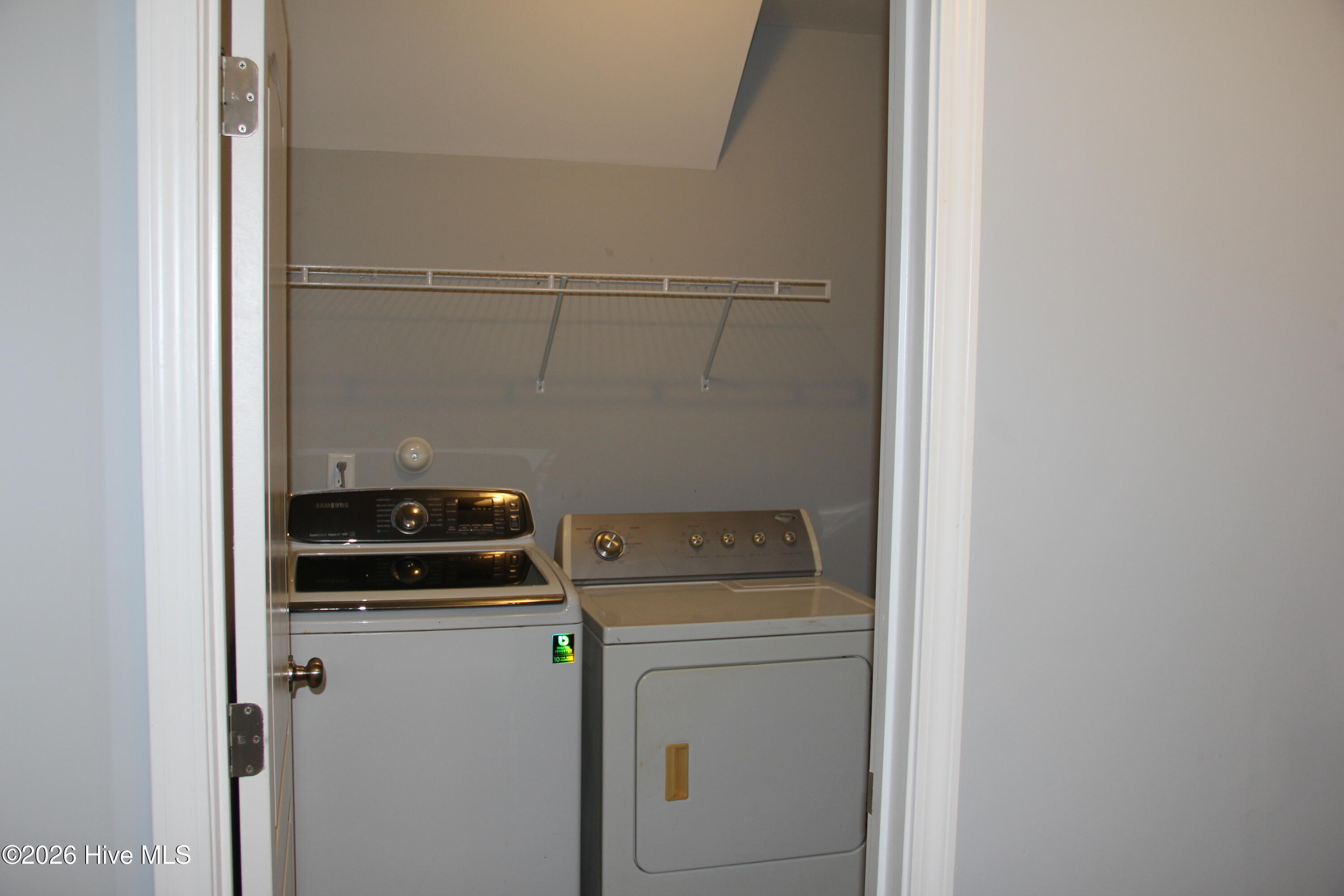 Laundry closet with a top-loading washer, front-loading dryer, and wire shelf.