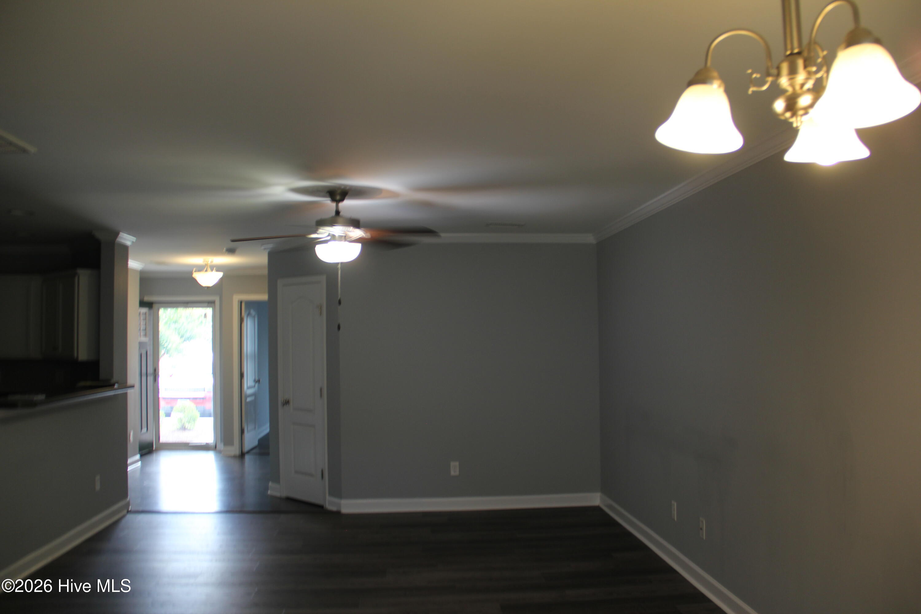 Empty dining area with dark flooring, a ceiling fan, and a chandelier beside the kitchen.