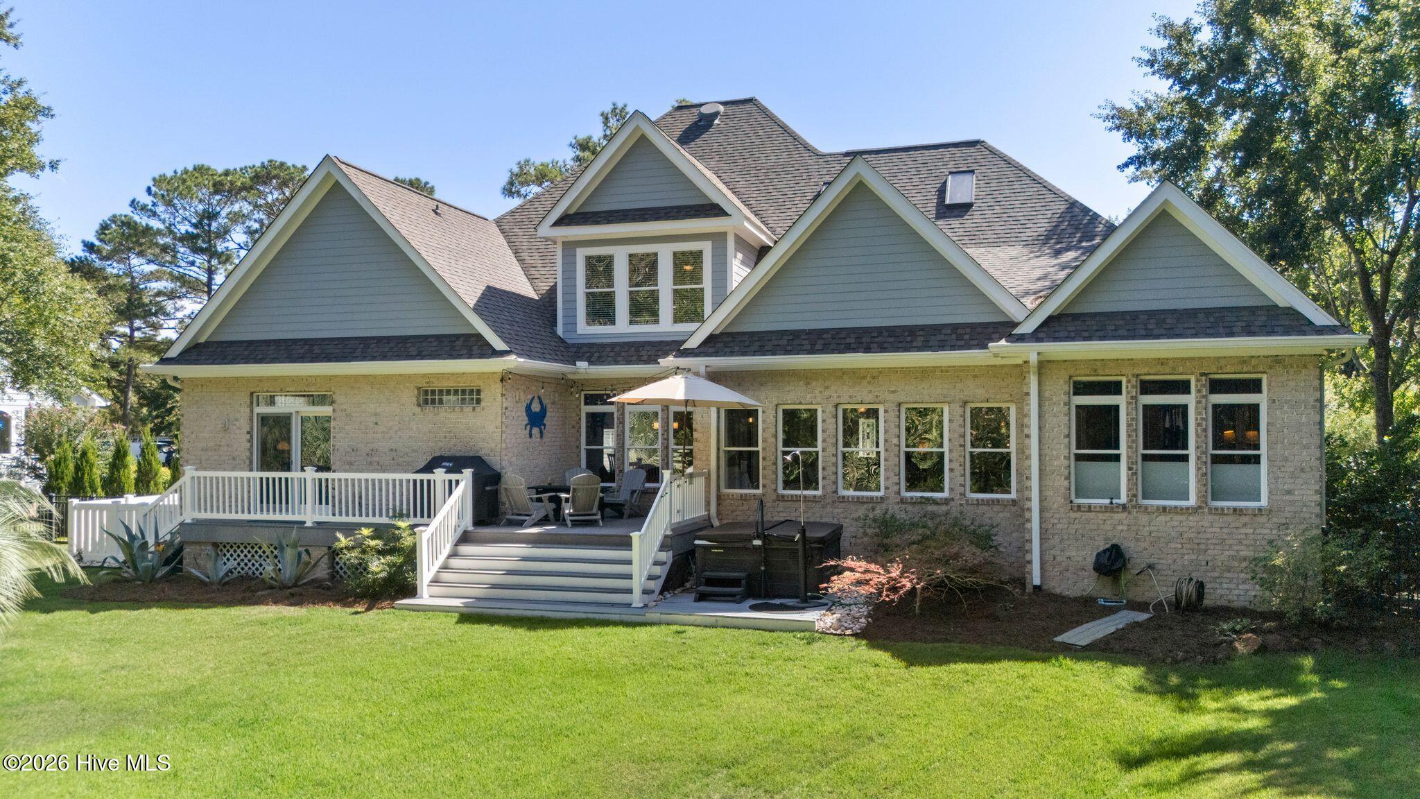 House rear exterior with a raised white deck, patio seating, and a broad green lawn.